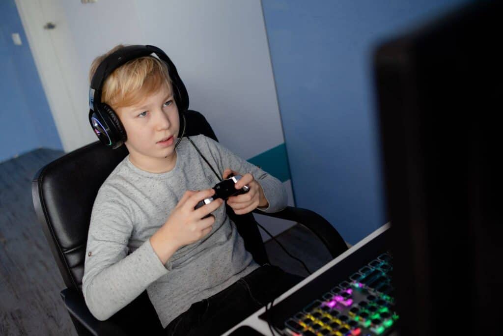 Young boy playing video games with headphones at a computer desk.