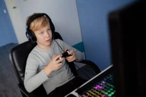 Young boy playing video games with headphones at a computer desk.